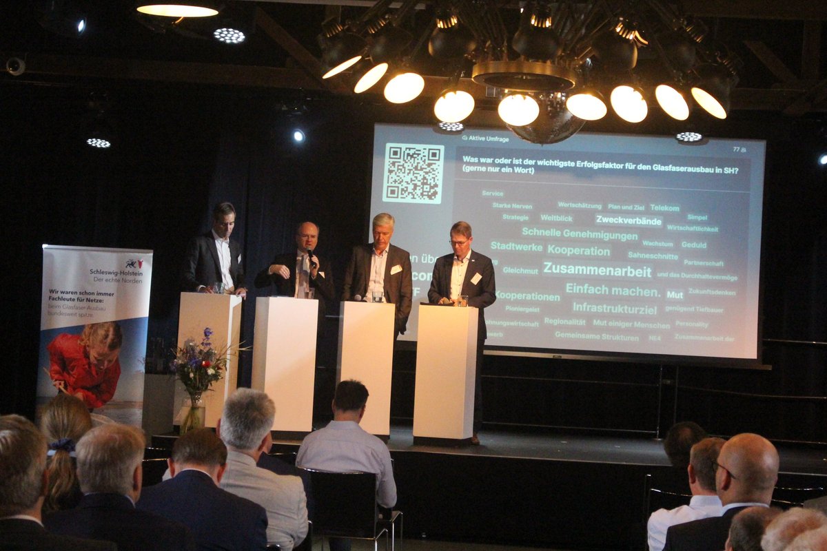 Jörg Bülow (Vorstandsvorsitzender des BKZ.SH), Johannes Hartwig (MWVATT) und Erk Westermann-Lammers (Vorstandsvorsitzender der IB.SH) und Dr. Klaus Winkler stehen beim 15. Glasfaserforum auf der Bühne. Foto: Maxim Schmuck